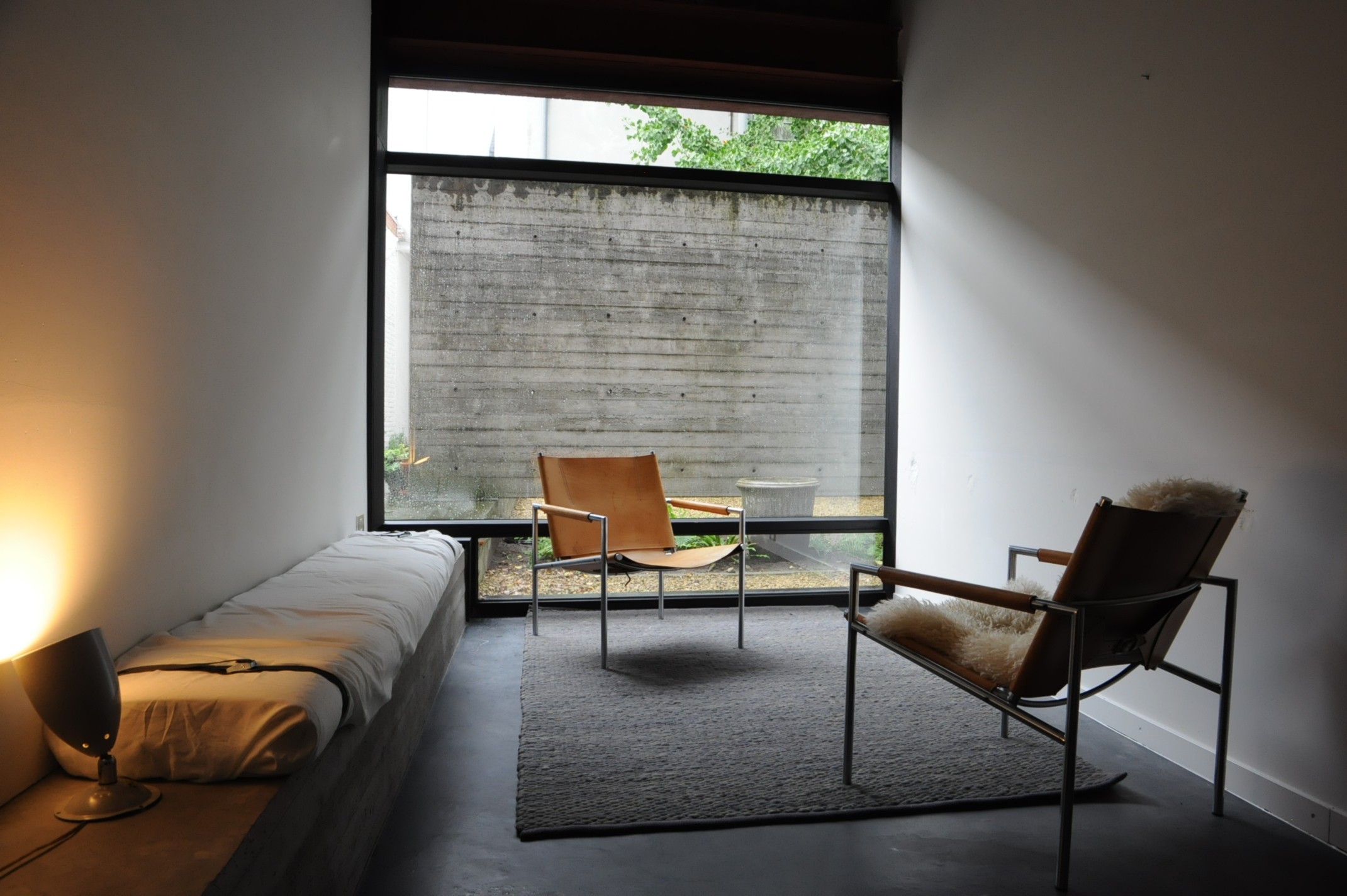 En studio met een houten vloer, zigzag patroon. Enkele donkergroene, stijlvolle stoelen voor een grote raampartij.
